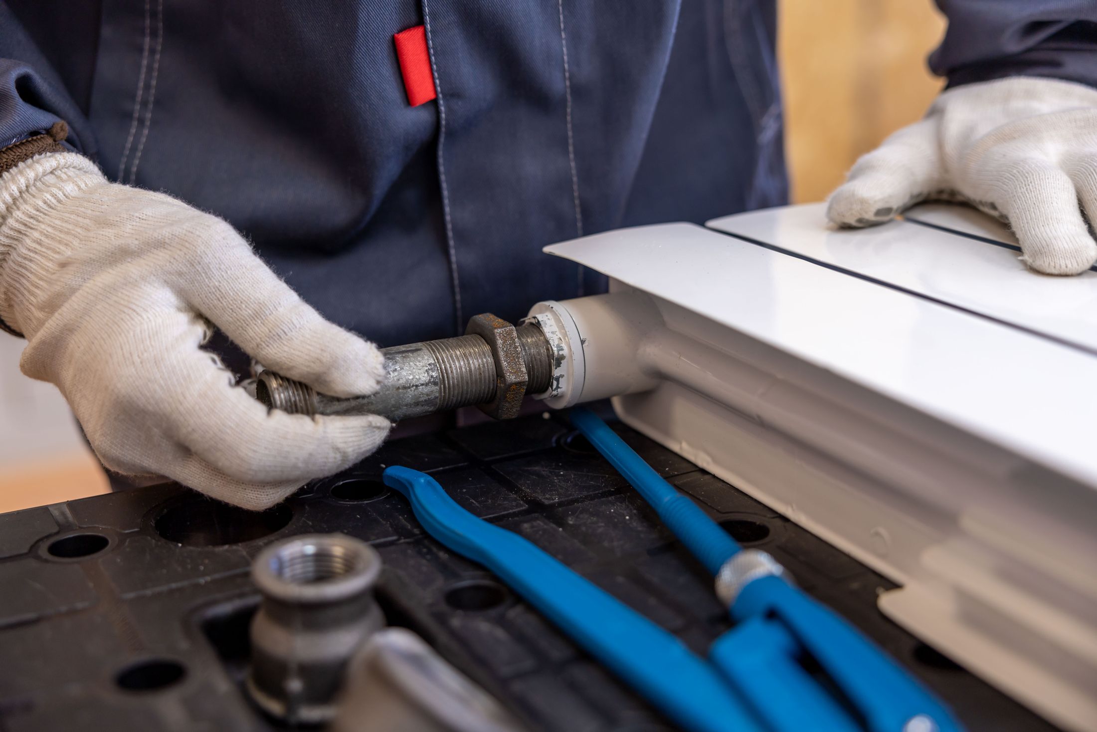 Gloved hands assembling a radiator pipe connection at a workbench — illustrative heating installation context